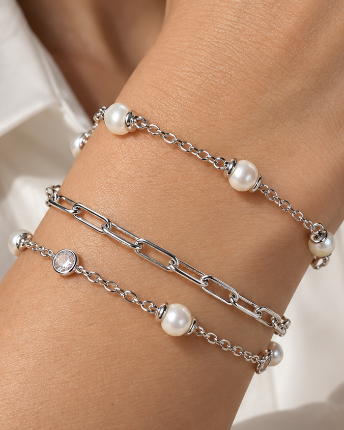 Silver-tone pearl, paperclip and zircon bracelets stacked on a wrist