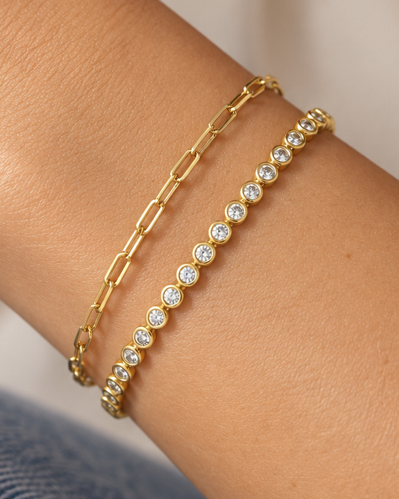 Gold-tone paperclip and zircon bracelets worn together on a wrist